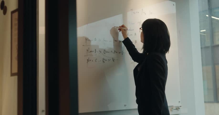 Woman writes on a whiteboard inside a welllit corporate room
