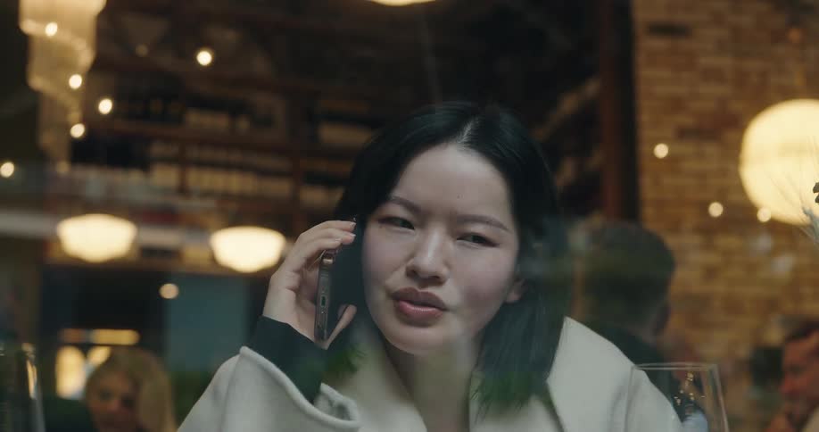 Woman on the phone in a busy restaurant seen through the window