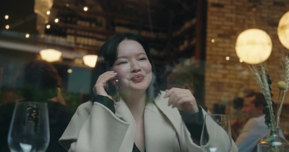 Close up of a young asian woman making a phone call while sitting at a table in a restaurant