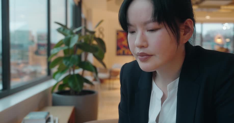 Woman adjusts and begins to remove her glasses while working on a laptop in an office setting