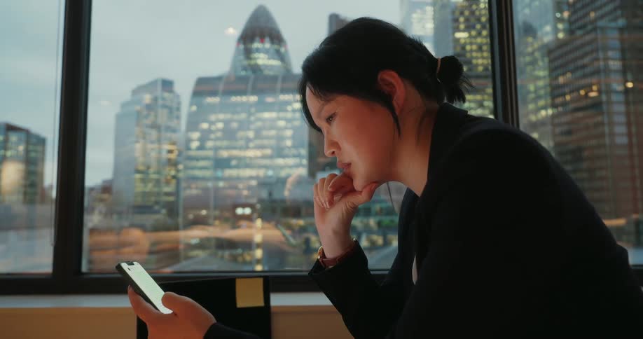 A woman sitting in a room texting on a phone