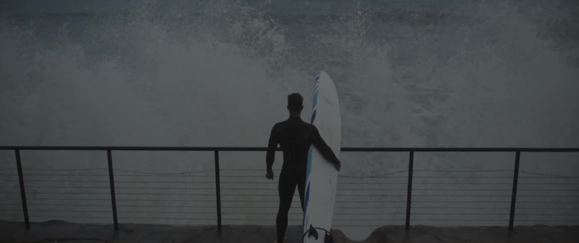 Waves splash up by a main carrying a surfboard