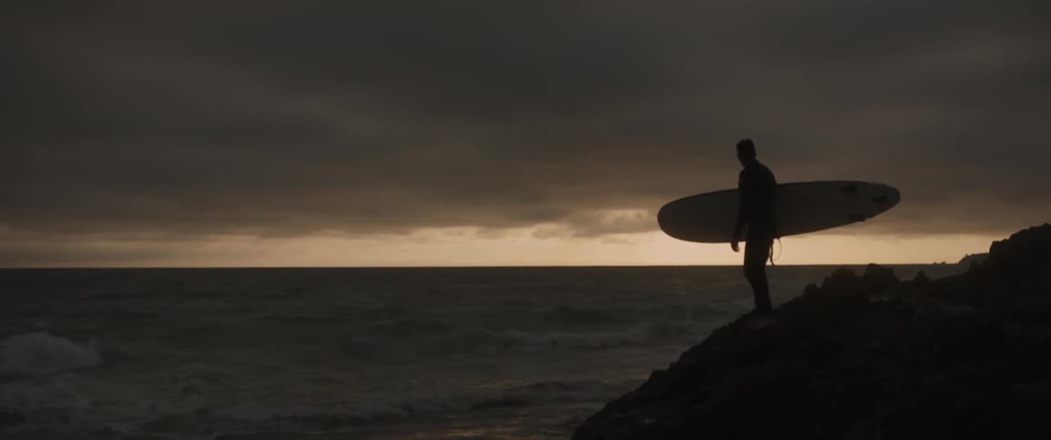 Man holding surfboard standing near beach after sunset
