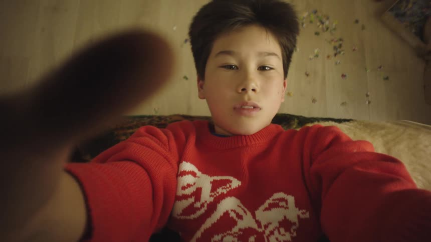 Child lying on the floor looks at the camera while reaching a hand forward