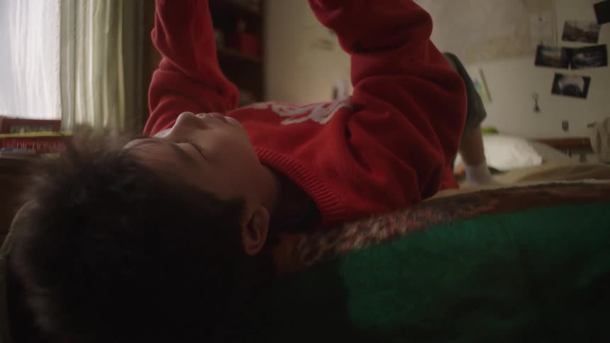Boy lies on the bed using a phone held above his face