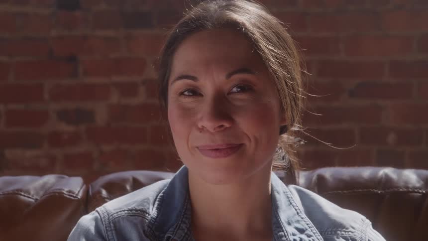 Woman sitting on a leather couch smiles softly under natural light