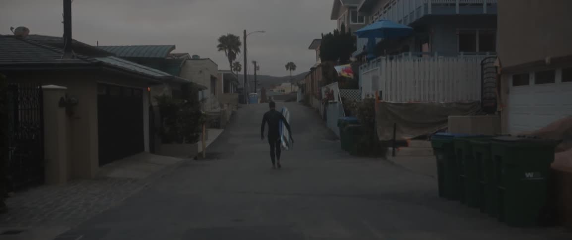A man walks down a road carrying a snowboard