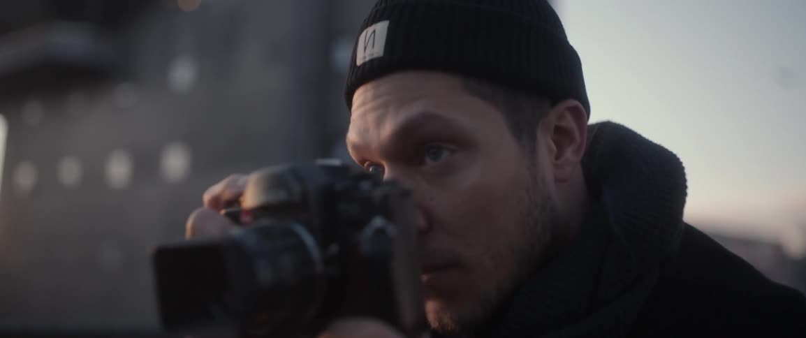 A man in a beanie raises a camera to his face