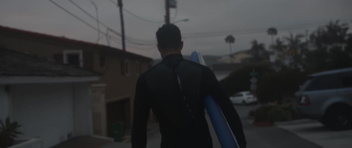 A man carries his surfboard past some houses