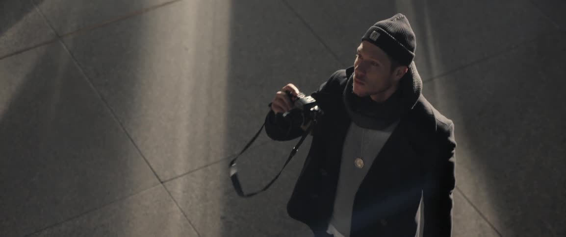 A man standing outside holds a camera up and looks through the viewfinder