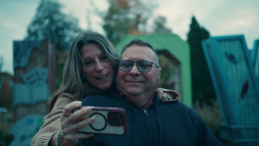 A smiling couple takes a selfie in an outdoor park at dusk