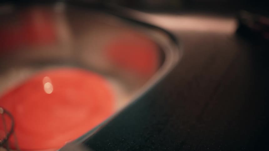A person sprays cleaner onto a countertop next to a sink and wipes it down