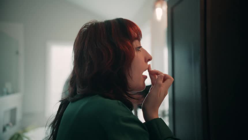 A woman standing in front of a mirror applying lip balm on her lips