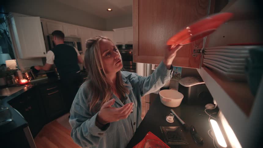 The man and woman are putting dishes into the cabinets