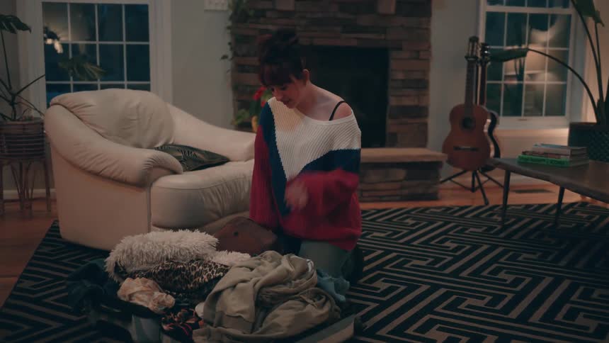 Woman kneeling beside an open suitcase full of clothes in a cozy living room