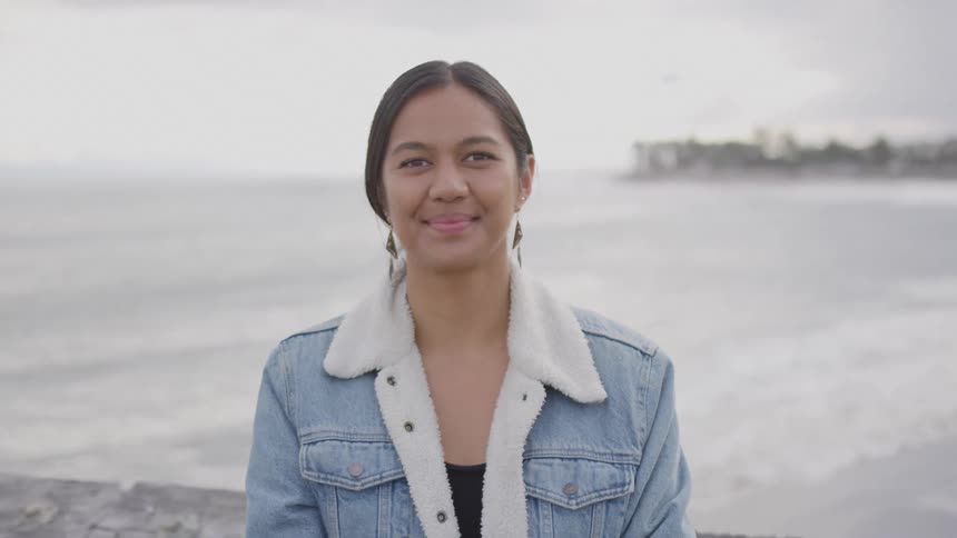 Woman smiles in front of the ocean wearing a denim jacket with a fuzzy collar