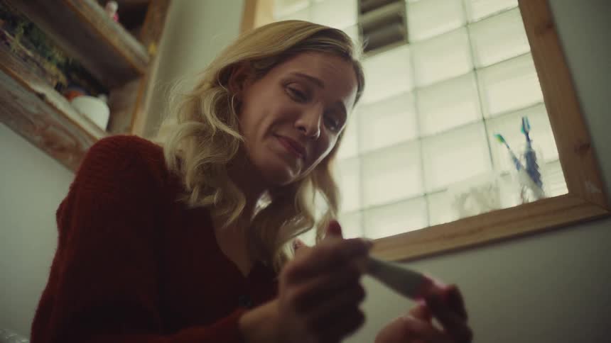 Woman smiles emotionally while looking at the result of the pregnancy test in her hands