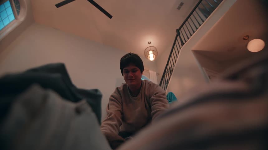 Man folds clothes while holding up a garment indoors