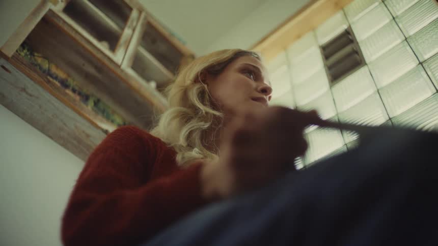 A young woman sits on a toilet seat looking at a pregnancy test tube with surprise