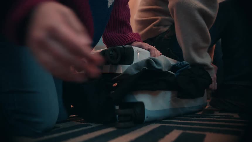 The man sits on the luggage in an attempt to close it