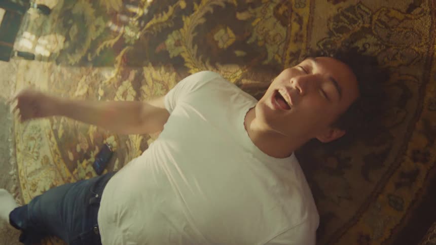 Man lying on a rug holding a phone and smiling