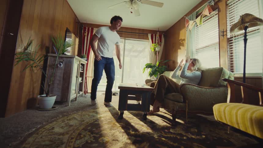 A man and a woman are sitting in a cozy woodpaneled living room they appear to be playing a game with dice on a low tablethe man suddenly jumps up excitedly pumping his fist and cheering suggesting he just made a winning move while the woman laug