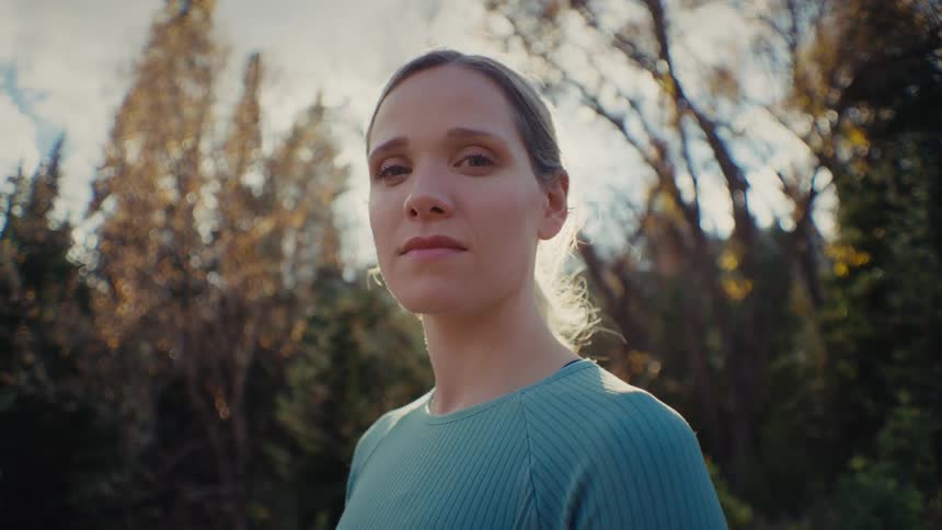 Young adult woman standing next to a forest outdoors during day time