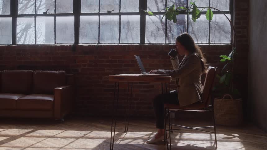 The woman drinks from a mug while using her laptop