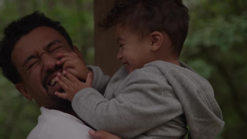 A man is holding a child with an intense joyful expression looking forward against a blurry green background