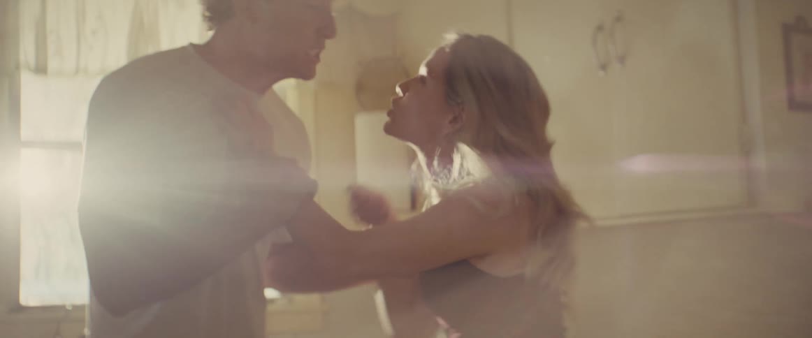 In a brightly overexposed indoor space a man and a woman are seen in close tense proximity leaning in toward each other as if in a heated discussion