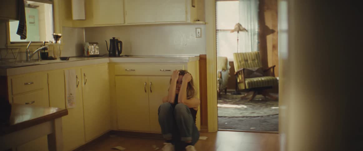 Woman sitting on the kitchen floor cries with a distressed expression