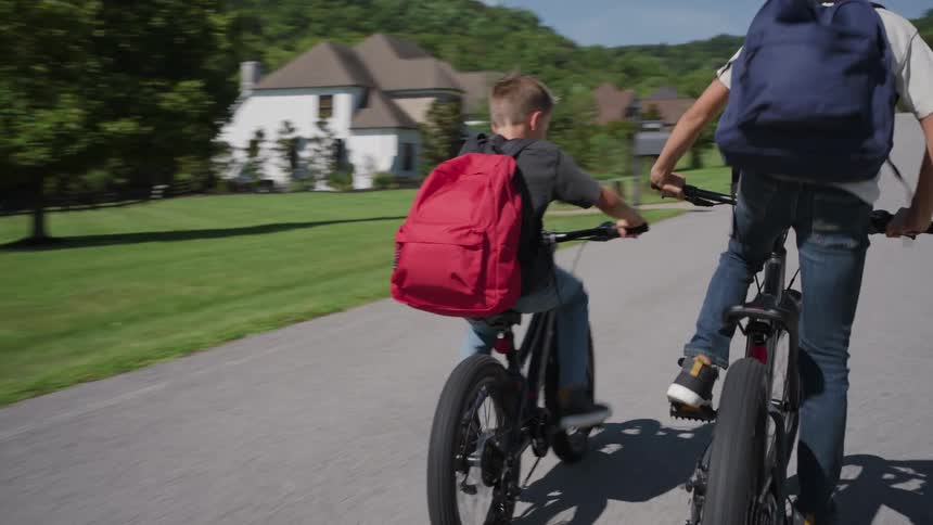 Two boys riding home from school on thier bikes through a residential neighborhood