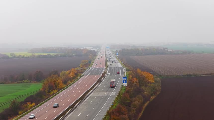 Aerial view of vehicles moving on a highway through foggy farmland under overcast sky