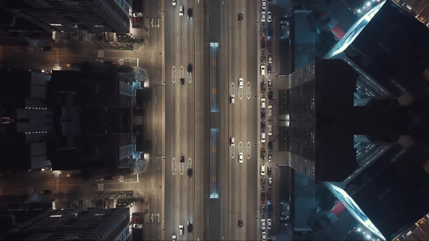 An abstract vertical mirrored view of a busy city freeway at night surrounded by dark buildings and bright street lights