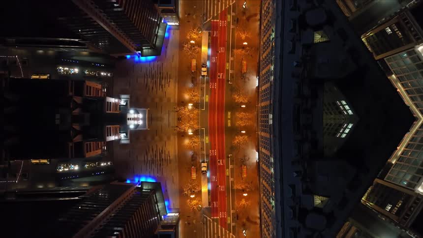 This is a psychedelic topdown drone shot of a city street at night heavily mirrored along the central axis the composition shows two identical illuminated sides of a metropolitan area with tall buildings flanking a central road marked with red taxi