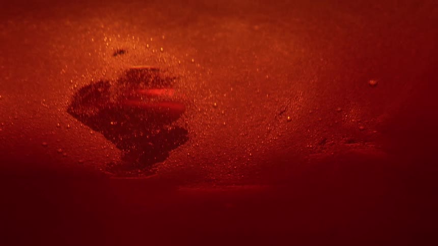 A red metallic fluid is oozing and moving in the light