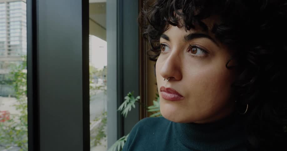 A woman stands by a window examining a small wind turbine model in an office