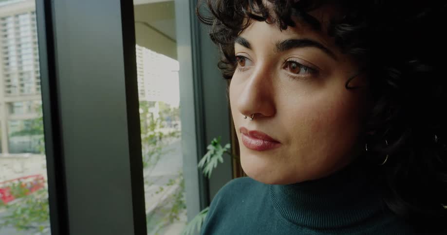A young woman stands by a large window in a modern office