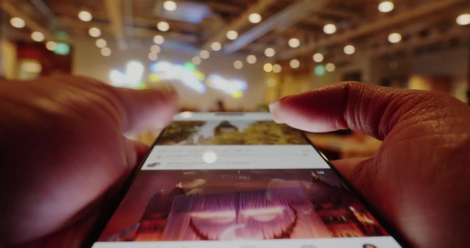 A close view of a person using a smartphone to scroll through content indoors under bright ceiling lights