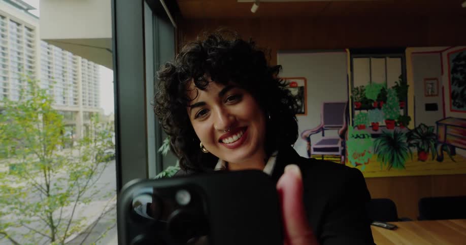 The face of a young woman who is holding a cell phone and while she is looking at it and waving