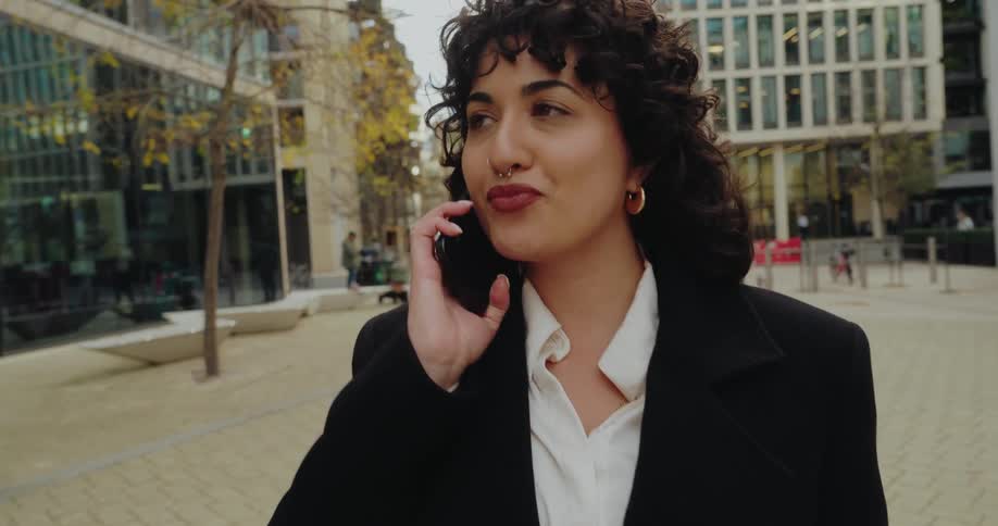A woman is on a city sidewalk and answers her celllphone