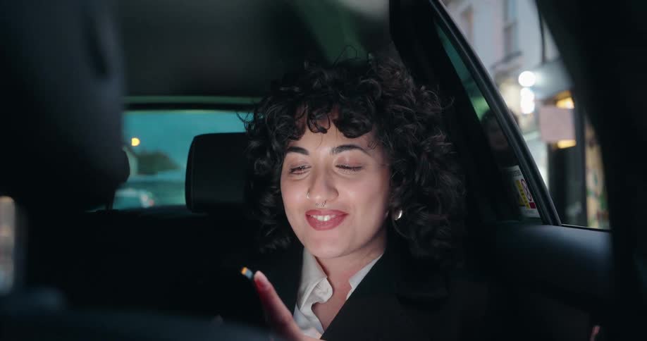 Woman smiles while using her phone in the back seat of a car at night
