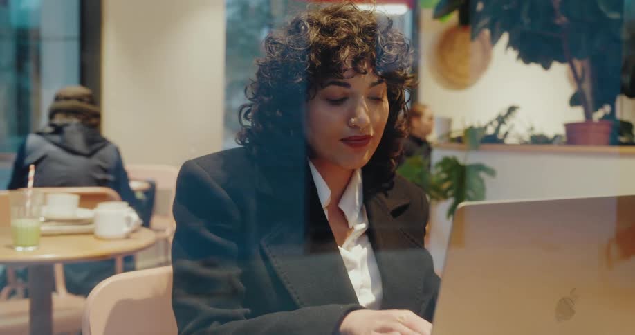 A woman sitting in a cafe thinks before typing on her laptop