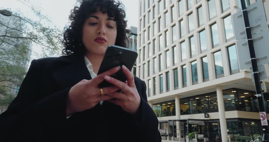 A woman wearing a black blazer is walking down a street using her cell phone