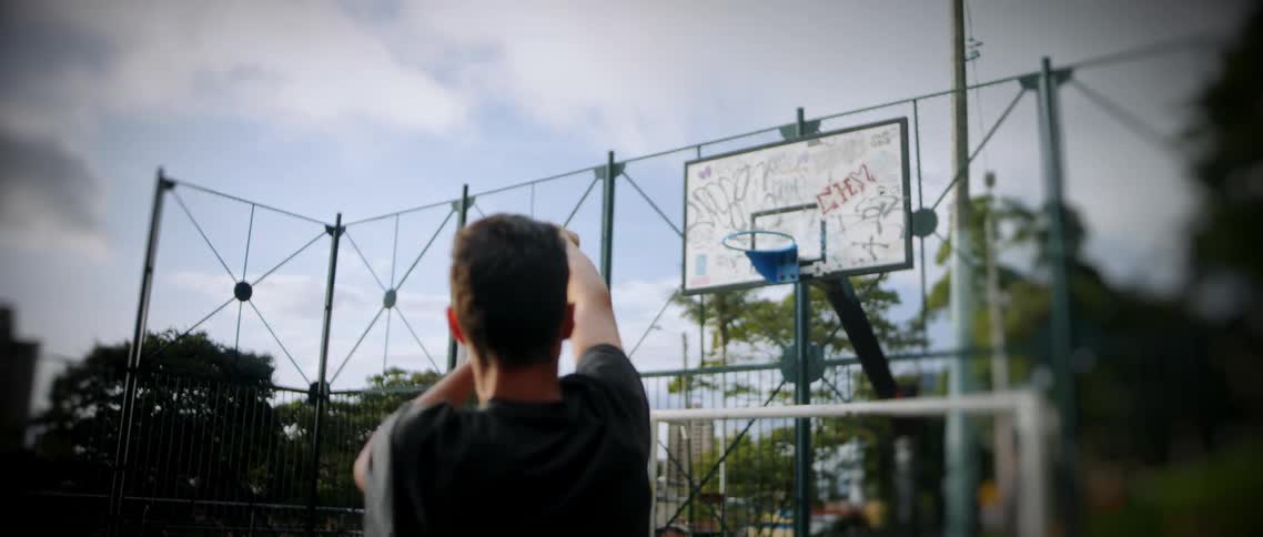 A young man tosses a basketball toward the hoop on a basketball court at midday
