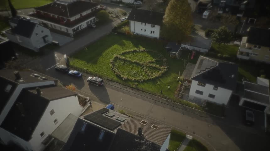 An aerial view of a suburban neighborhood with a circular pattern in a backyard lawn