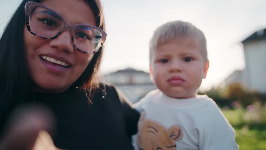 Woman wearing glasses holds a child outdoors under soft light