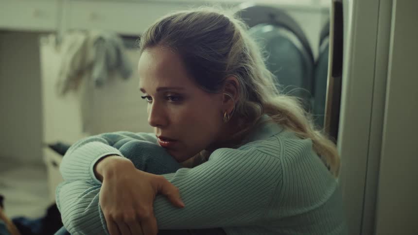 Woman sitting hugs her knees with a sad expression
