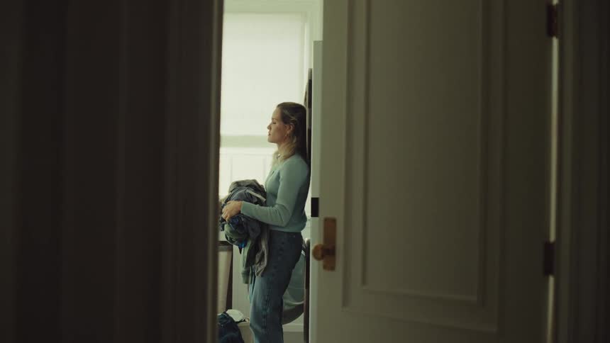 Woman stands in a room of the house looking dejected