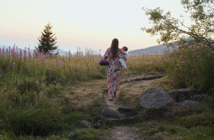 Woman walking along a flowerlined path while carrying a child
